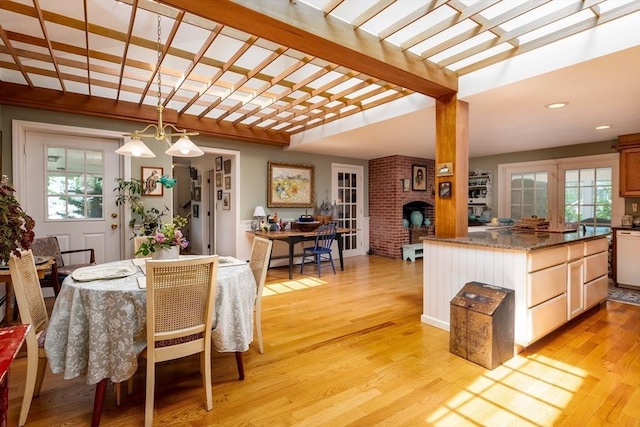 dining room featuring a brick fireplace, beam ceiling, light hardwood / wood-style flooring, and french doors