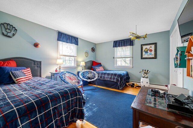 bedroom with multiple windows, wood-type flooring, a textured ceiling, and baseboard heating