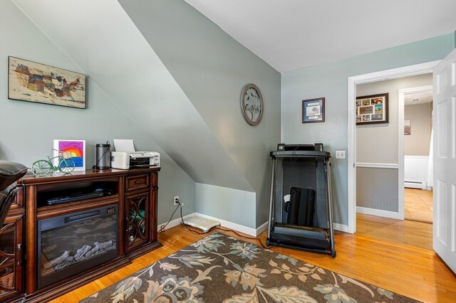 living area featuring lofted ceiling, a baseboard heating unit, and hardwood / wood-style flooring