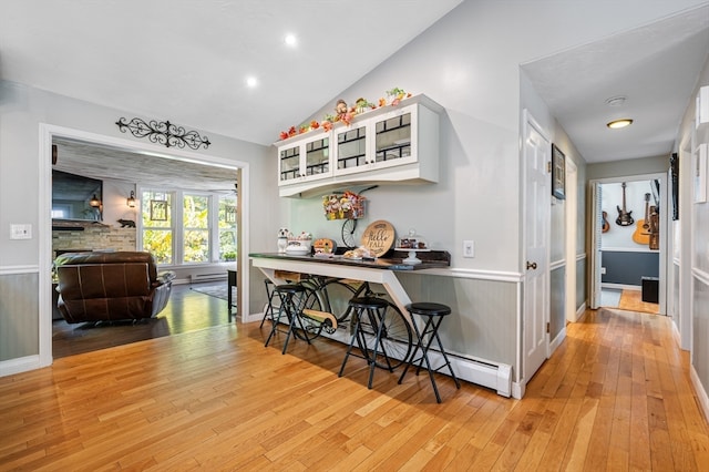 interior space with a baseboard radiator, white cabinets, lofted ceiling, and light wood-type flooring