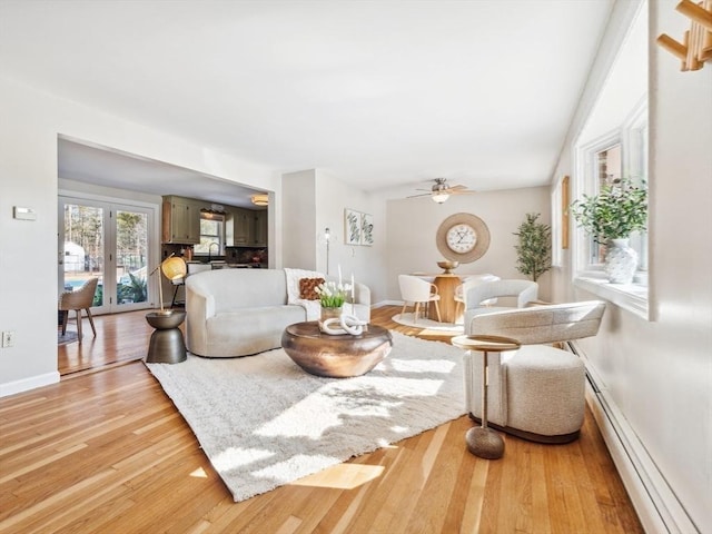 living area with light wood finished floors, a baseboard heating unit, baseboards, french doors, and a ceiling fan