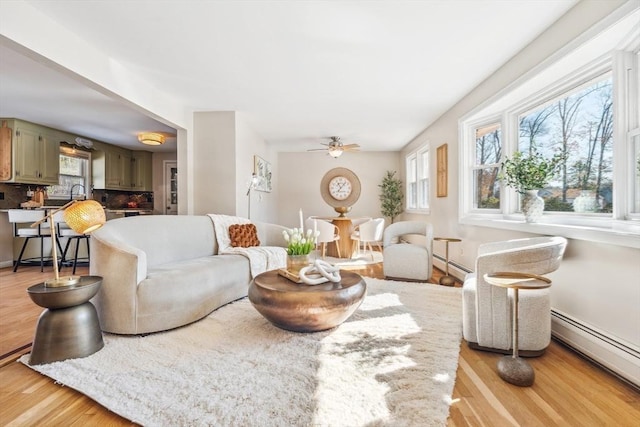 living room featuring light wood-style flooring, a baseboard heating unit, and ceiling fan