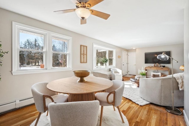 dining area with a baseboard heating unit, a ceiling fan, and wood finished floors