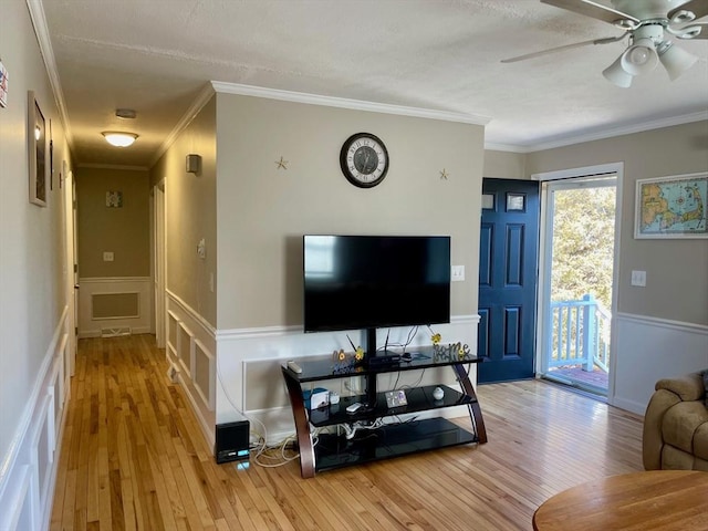 living area with a wainscoted wall, ceiling fan, hardwood / wood-style floors, and crown molding