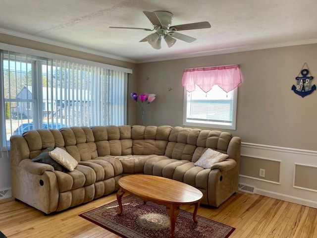 living room featuring light wood-style floors, a wainscoted wall, a healthy amount of sunlight, and crown molding