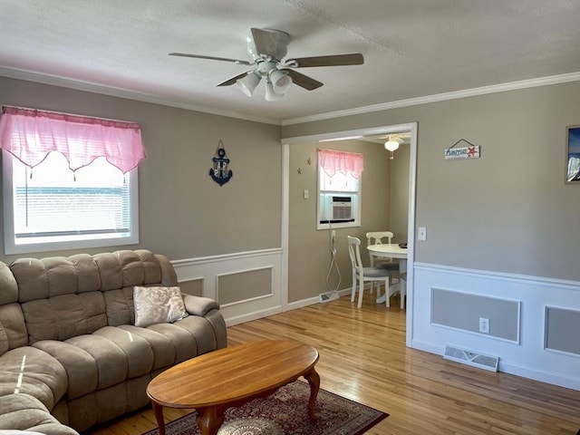 living area with light wood-type flooring, visible vents, crown molding, and wainscoting