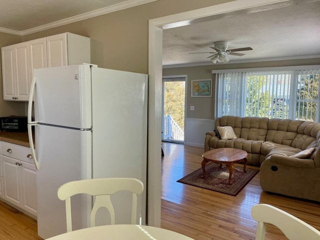 kitchen with freestanding refrigerator, white cabinets, crown molding, and light wood-style flooring