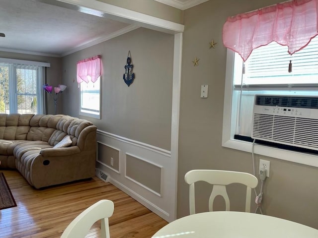 living room with ornamental molding, cooling unit, a wainscoted wall, and light wood-style flooring