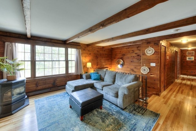 living room featuring a wood stove, wood walls, light wood-style flooring, a baseboard radiator, and beamed ceiling