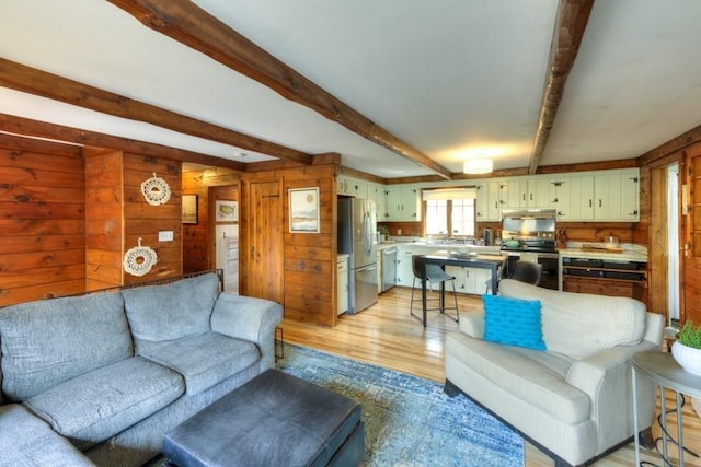 living area with light wood-type flooring, wood walls, and beam ceiling