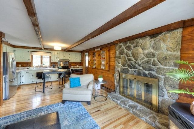 living area with wooden walls, beamed ceiling, light wood finished floors, and a stone fireplace