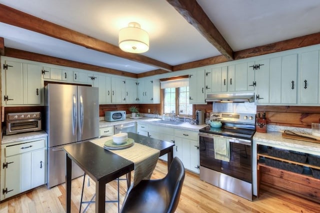 kitchen with beam ceiling, light countertops, under cabinet range hood, light wood-style flooring, and stainless steel appliances