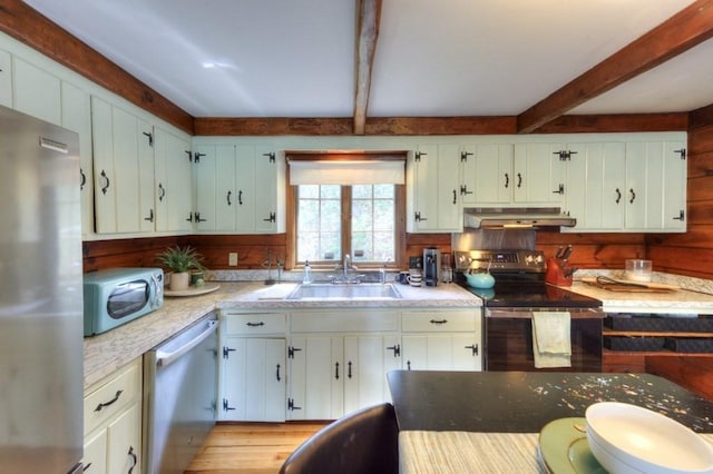 kitchen with beam ceiling, light wood-style floors, under cabinet range hood, a sink, and stainless steel appliances