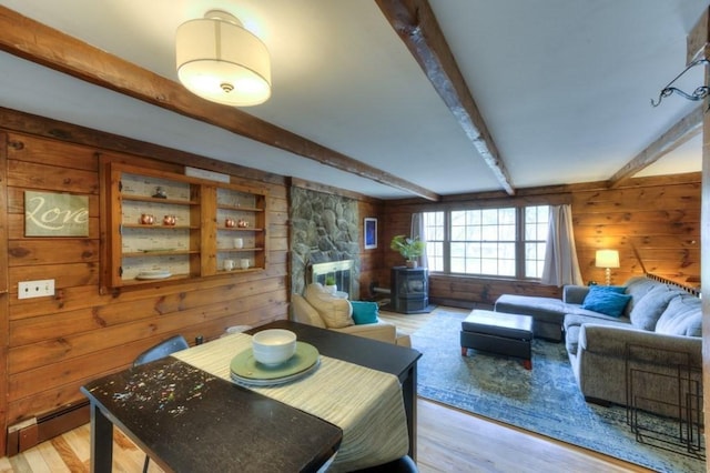 dining room featuring wooden walls, beamed ceiling, baseboard heating, and light wood-style floors