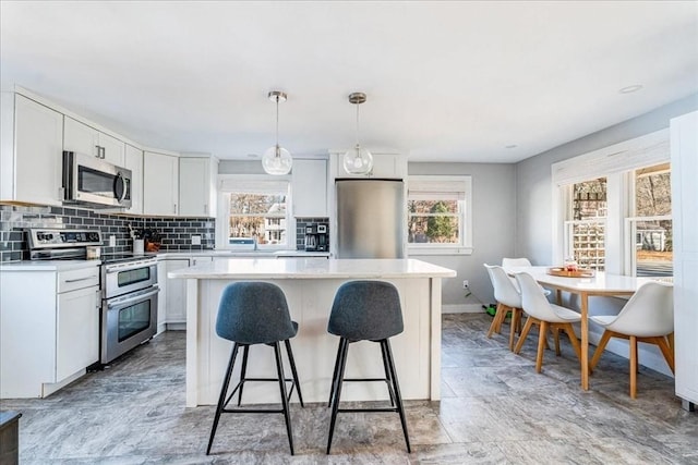 kitchen with white cabinetry, a kitchen island, hanging light fixtures, and appliances with stainless steel finishes