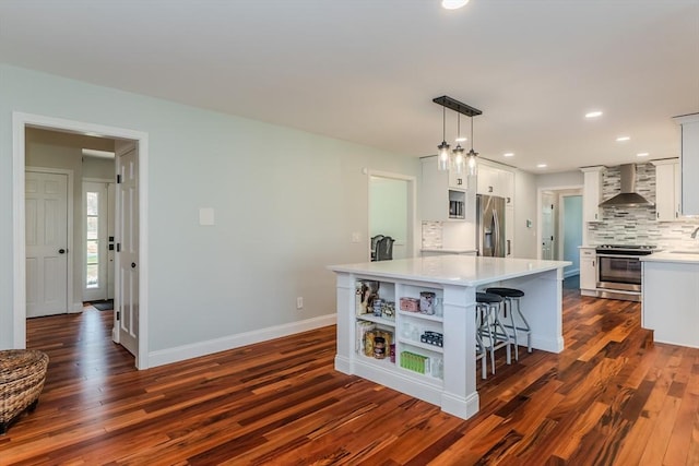 kitchen with dark wood-style floors, a center island, light countertops, wall chimney exhaust hood, and appliances with stainless steel finishes