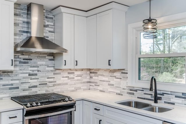 kitchen featuring wall chimney range hood, a sink, gas stove, white cabinetry, and backsplash