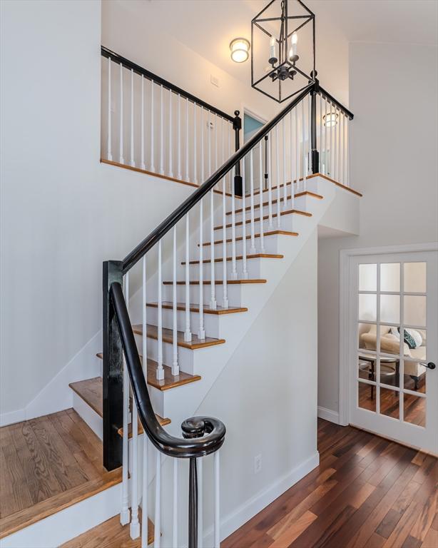 staircase with baseboards, a towering ceiling, wood finished floors, and a notable chandelier