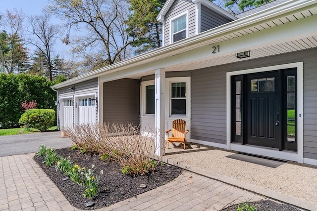 view of exterior entry featuring a porch, an attached garage, and aphalt driveway