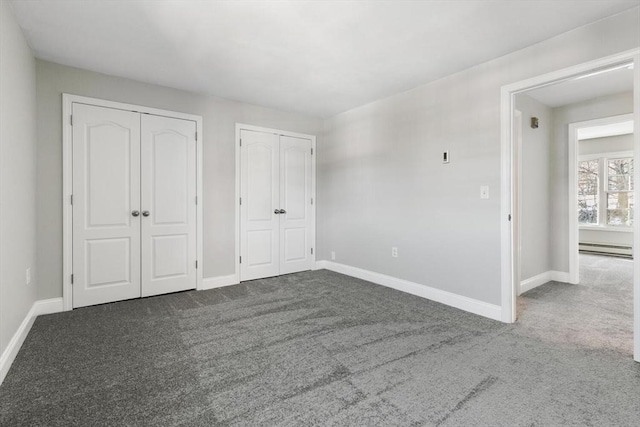 unfurnished bedroom with a baseboard heating unit, two closets, and carpet flooring