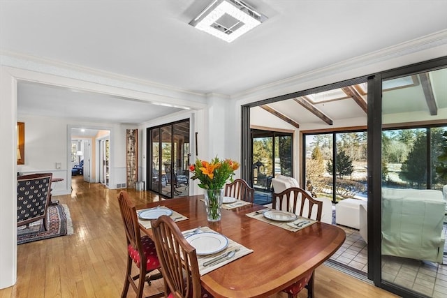 dining space featuring beam ceiling, crown molding, light hardwood / wood-style floors, and a skylight