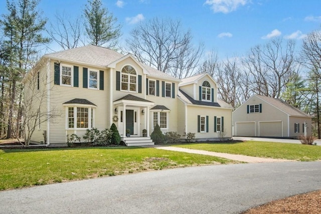 colonial home featuring a garage, a front yard, and an outdoor structure