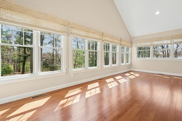 unfurnished sunroom featuring high vaulted ceiling, baseboards, visible vents, and hardwood / wood-style flooring