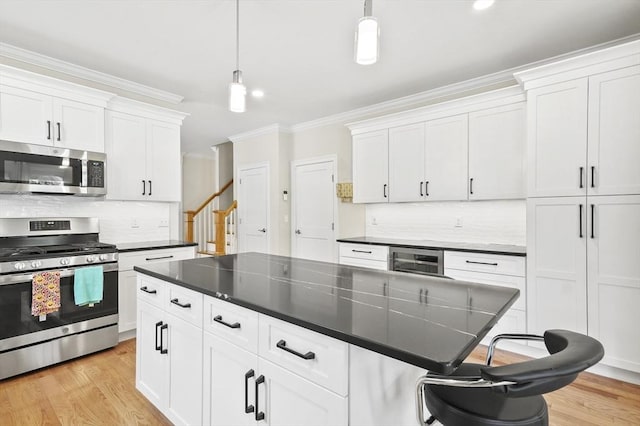 kitchen with crown molding, stainless steel appliances, dark countertops, light wood-style floors, and white cabinetry