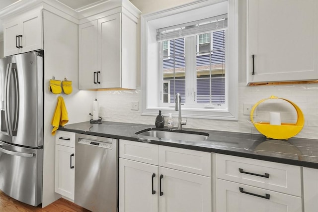 kitchen with appliances with stainless steel finishes, white cabinets, a sink, and tasteful backsplash