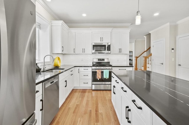 kitchen with dark countertops, light wood-style flooring, appliances with stainless steel finishes, crown molding, and a sink