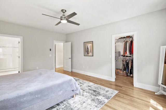 bedroom with baseboards, ensuite bath, a walk in closet, light wood-style floors, and a closet