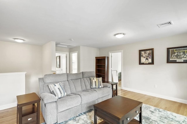 living area with attic access, baseboards, visible vents, and light wood finished floors