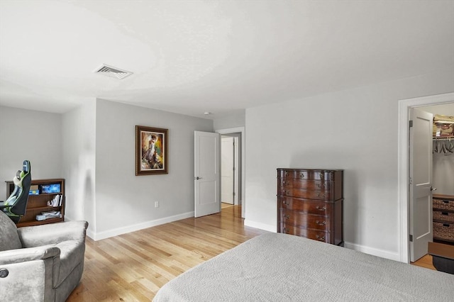 bedroom featuring a walk in closet, wood finished floors, visible vents, and baseboards