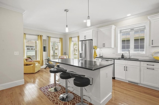 kitchen with dark countertops, a breakfast bar area, appliances with stainless steel finishes, ornamental molding, and a sink