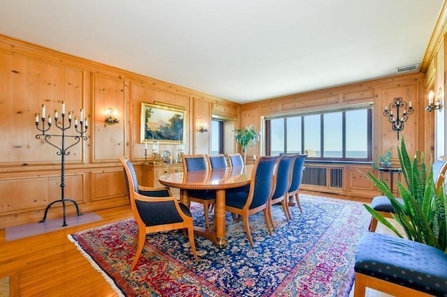 dining area with radiator heating unit, wood walls, and light hardwood / wood-style floors