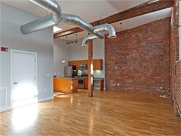 unfurnished living room with beamed ceiling, brick wall, a towering ceiling, and light wood-type flooring