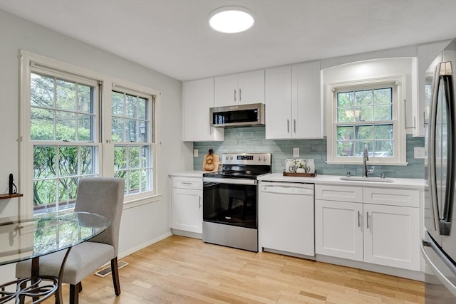 kitchen with stainless steel appliances, a sink, light countertops, and light wood finished floors