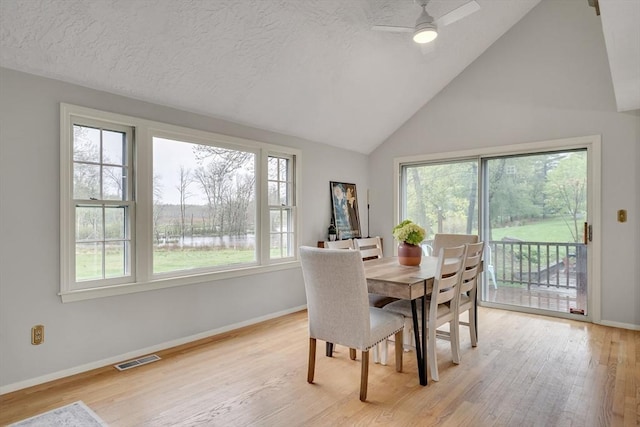 dining room featuring light wood-style flooring, baseboards, ceiling fan, high vaulted ceiling, and a textured ceiling