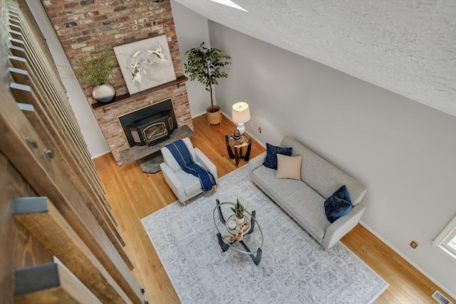 living area featuring wood finished floors, a textured ceiling, baseboards, lofted ceiling, and a wood stove