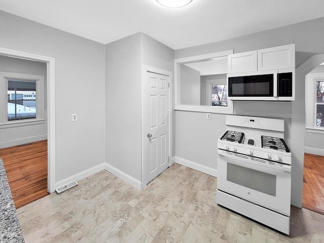 kitchen with white cabinetry, white appliances, and light hardwood / wood-style floors