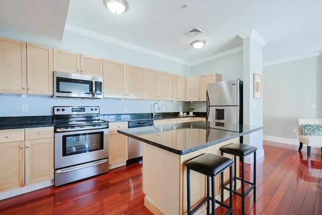 kitchen featuring a kitchen island, dark hardwood / wood-style flooring, stainless steel appliances, crown molding, and a breakfast bar area