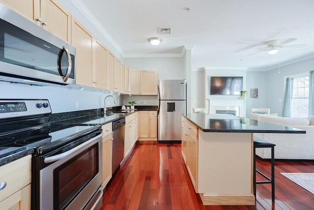 kitchen with appliances with stainless steel finishes, a center island, ornamental molding, a breakfast bar, and sink