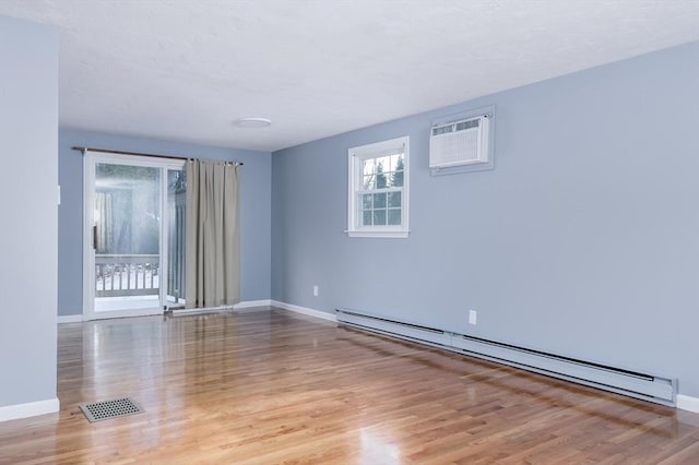 empty room featuring an AC wall unit, a baseboard heating unit, and light hardwood / wood-style floors