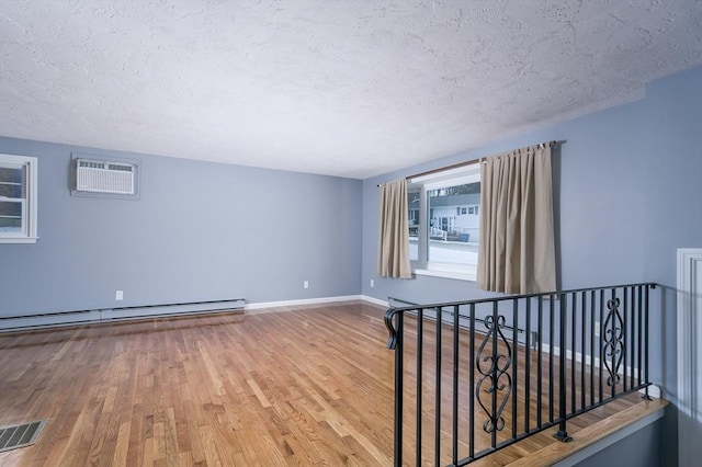 spare room featuring a textured ceiling, hardwood / wood-style floors, a wall unit AC, and a baseboard heating unit