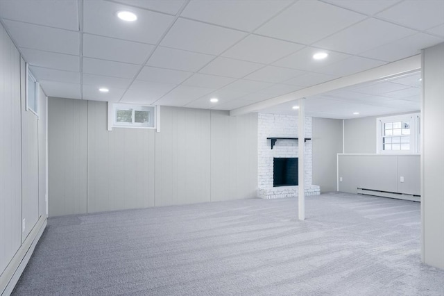 basement with light colored carpet, a brick fireplace, and a baseboard heating unit