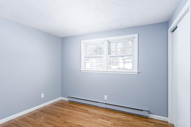 spare room with baseboard heating, a textured ceiling, and light hardwood / wood-style flooring