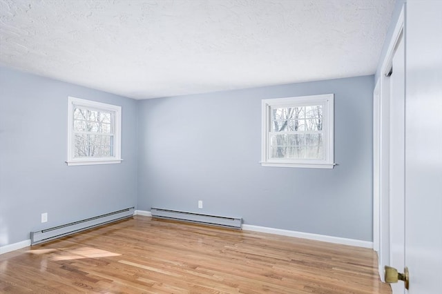 unfurnished room with a baseboard heating unit, plenty of natural light, and light hardwood / wood-style flooring