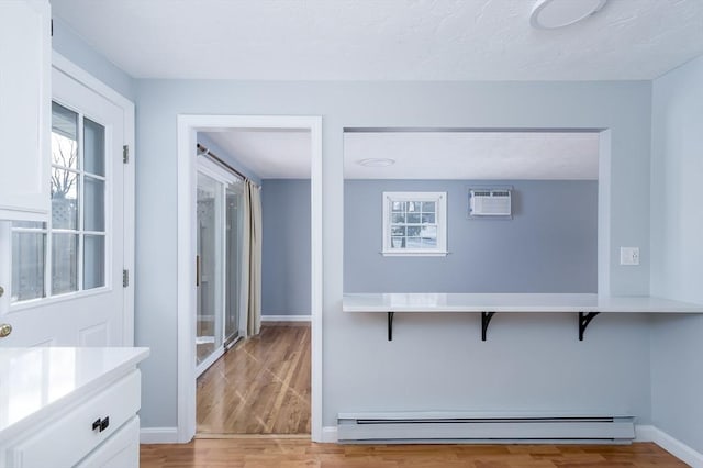 kitchen featuring an AC wall unit, white cabinets, a baseboard radiator, and light hardwood / wood-style flooring