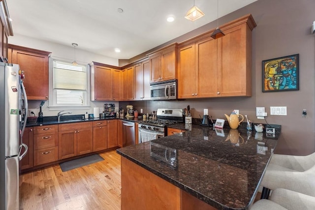 kitchen featuring appliances with stainless steel finishes, a peninsula, light wood-style flooring, brown cabinetry, and recessed lighting