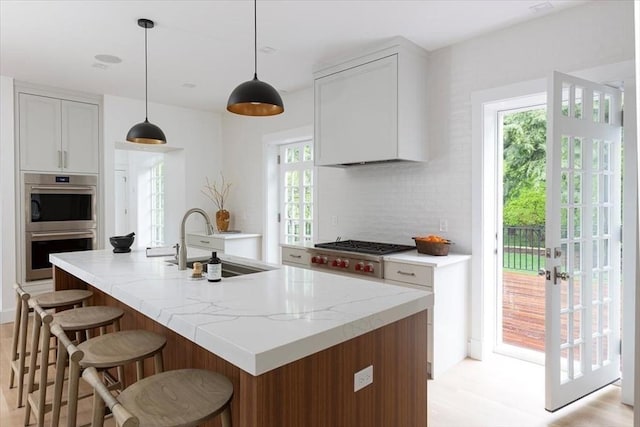 178 Ivy St, Brookline, MA 02446 - kitchen featuring a sink, appliances with stainless steel finishes, a breakfast bar area, decorative backsplash, and a kitchen island with sink